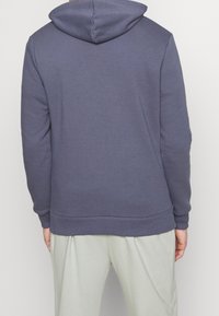 Felpa con cappuccio di colore grigio scuro, realizzata in tessuto morbido; presenta polsini e orlo a coste. Cuciture visibili sul retro, design minimale.