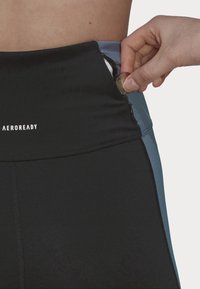 Leggings atletici neri a vita alta con pannello laterale blu, dotati di tasca con zip per monete e vita regolabile.