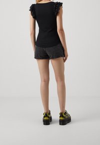 Černý bezrukávový top s volány na ramínkách, spárovaný se šedými denimovými šortkami a robustními černými platformami s žlutými akcenty.