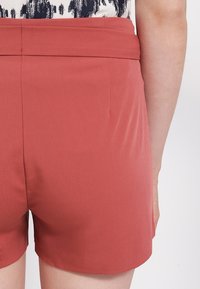 Pantaloni corti color ruggine realizzati in tessuto morbido, con una vita aderente e un design pulito e semplice senza abbellimenti visibili.