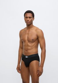 Zwarte katoenen slip met elastische tailleband en een gestructureerd logo. Het design is aangesloten en zorgt voor een gladde silhouet.