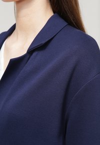 Marinblå kavaj med en slät yta, med notched krage och strukturerade axlar, som visar en närbild av tyget och designen.