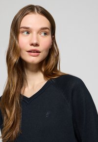 Granatowy sweter w serek wykonany z miękkiego materiału, z delikatnym logo na klatce piersiowej oraz teksturowanymi akcentami na rękawach.