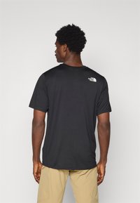 T-shirt noir à manches courtes avec un col rond. Dispose d'un petit logo blanc sur le haut du dos. Tissu lisse et coupe décontractée.