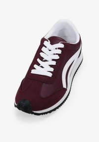 Zapatilla deportiva color marrón burdeos con parte superior de material sintético, cordones blancos y suela de goma con un patrón de relieve. Acentos lisos y texturizados.