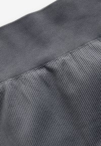 Tessuto a coste grigio con superficie texturizzata, dotato di una cintura larga. Il materiale appare morbido e leggermente elasticizzato.