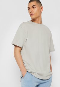 Tricou gri cu mâneci scurte, cu o croială lejeră, guler rotund și textură moale. Asortat cu pantaloni bleu deschis, cu mâinile în buzunare.