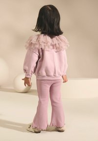 Sweat-shirt rose clair avec col en tulle froncé, associé à un pantalon évasé à côtes rose clair. Texture douce et coupe décontractée.