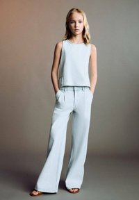 Lichtblauw crop-top zonder mouwen met een rechte snit en korte mouwen, gecombineerd met lichtblauwe denim broeken met wijde pijpen en zijzakken.