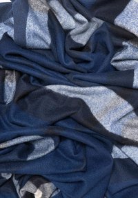 Niebiesko-szaro wzorzysty szalik wykonany z miękkiego materiału, z różnymi odcieniami o teksturowanym wykończeniu, ułożony w sposób pokazujący jego przepływ i formę.