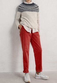 Pull en maille ivoire avec yoke à motif bleu foncé, associé à un pantalon en velours côtelé rouge et des baskets blanches avec des accents gris. Tenue décontractée présentée.