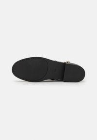 Semelle noire d’une chaussure à talon plat estampillée « MICHAEL KORS », avec des zones de grip texturées et un talon carré lisse.