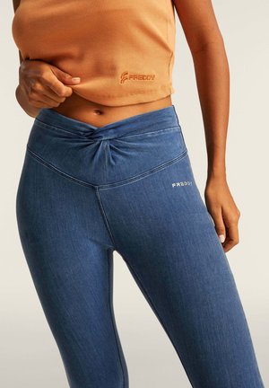 Leggings in denim con dettaglio in vita a nodo, di colore blu scuro. Il tessuto sembra elastico con cuciture tono su tono e un sottile logo decorativo.