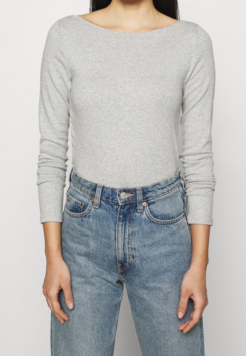 Svetle šedý top s dlouhým rukávem z měkkého materiálu, spojený s vyšším modrým džíny s vybledlým vzhledem a klasickým designem pěti kapes.