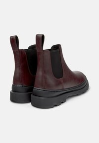 Stivali Chelsea in pelle bordeaux con inserti elasticizzati neri, linguette e una robusta suola in gomma nera. Texture liscia con dettagli di cucitura.