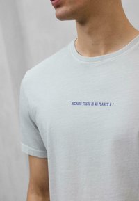 Camiseta de algodón gris claro con mangas cortas, con el texto azul "PORQUE NO HAY UN PLANETA B" centrado en el pecho. Textura suave.
