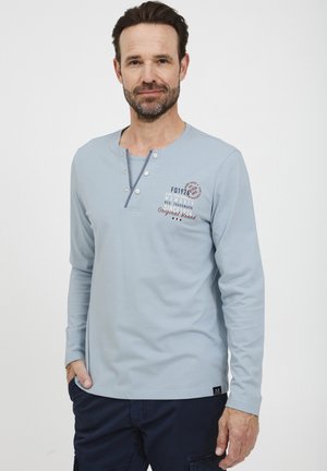 Light blue long-sleeve henley shirt with a round neckline, three-button closure, and printed text accents in dark red and gray.