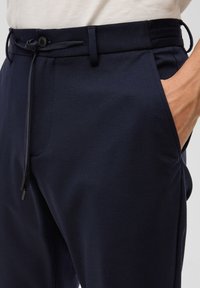 Navy-Hosen aus weichem Stoff mit einem Kordelzugbund, Seitentaschen und einer glatten Textur. Mit einem Knopfverschluss und gesteppten Details.