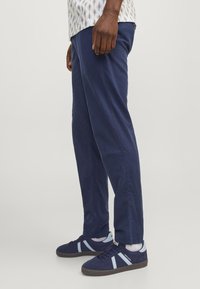 Laivastonsiniset suoralahkeiset puuvillahousut, yhdistetty laivastonsinisiin lenkkareihin, joissa on vaaleansinisiä yksityiskohtia ja tekstuuri mokkanahasta.