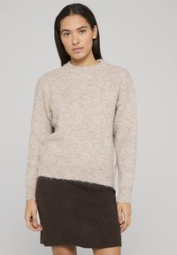Pull en tricot beige avec une finition texturée, col rond et épaules tombantes, associé à une jupe en tricot marron foncé avec un ourlet côtelé.