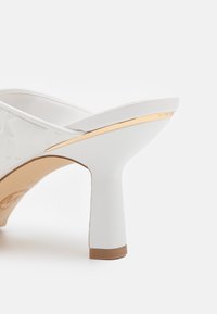 Bílé sandály na vysokém podpatku s lesklým povrchem, zdobené zlatým akcentem na podpatku a raženou strukturou na svrchní části.