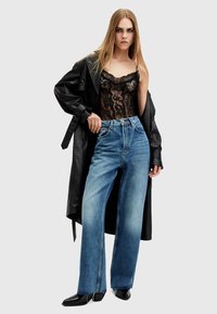 Abrigo largo de cuero negro, top de encaje y jeans de tiro alto y pierna ancha en azul. Detalles notables: patrón de encaje, denim deslavado, dobladillos con cremallera y botas negras de punta.