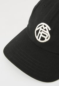 Sort baseball cap med et hvidt broderet cirkulært logo, der viser stiliserede bogstaver og geometriske former på frontpanelet.