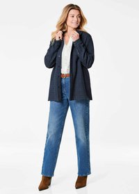 Dark blue button-up shirt with a textured fabric, paired with light blue straight-leg jeans and brown ankle boots. White blouse underneath.
