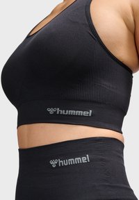 Zwarte sportbeha en leggings met ribbelstructuur en elastische taillebanden, met het 'hummel' logo in lichtgrijs op beide items.