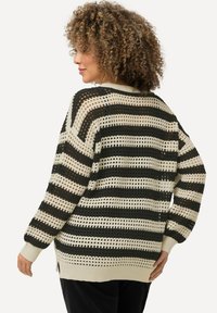 Maglione a righe lavorato a maglia con motivo a trama aperta, caratterizzato da righe alternate in nero e crema. I bordi sono a costine e presentano spacchi laterali.