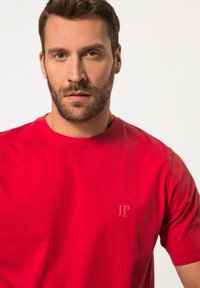 Röd bomull t-shirt med rund halsringning, korta ärmar och en liten JP-logga i en ljusare nyans på bröstet.