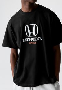Čierne bavlnené tričko s bielym logom Honda a textom "Civic Si" v oranžovej farbe. Klasický strih s okrúhlym výstrihom, voľný strih.