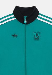 Chaqueta de chándal teal con cuello negro, cremallera completa, rayas blancas y teal de Adidas, con logos bordados de Adidas y Liverpool FC.