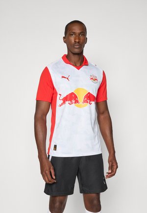 Hvid og rød fodboldtrøje med krave, der har en gul cirkel og to røde okser logo foran, parret med sorte shorts.