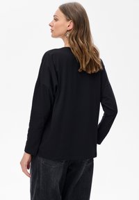 Czarny długi rękaw, luźna koszulka z okrągłym dekoltem i opadającymi ramionami, w połączeniu z ciemnymi dżinsami.