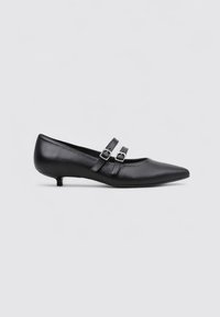 Zapato de cuero negro de tacón bajo con dos correas ajustables, punta afilada y textura suave. Presenta detalles de herrajes plateados.