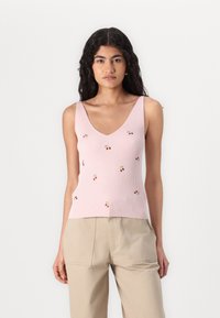 Top a righe rosa con scollatura a V e piccola ricamatura di ciliegia rossa. Indossato con pantaloni beige. Tessuto morbido e design aderente.