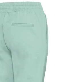 Ljust gröna joggerbyxor med elastisk midja, slät textur, sidofickor och en minimalistisk design med en enda bakficka.