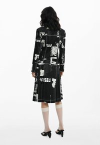Woman with wavy dark hair wears black-and-white abstract print jacket and pleated skirt, white knee-high sheer socks, and black heeled sandals.