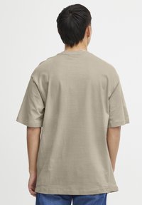 Beige bavlněné tričko s volným střihem, krátkými rukávy a kulatým výstřihem. Hladká textura, boční švy a rovný lem.