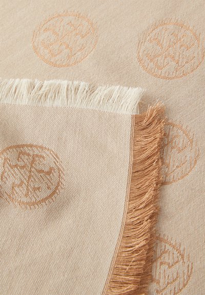 Lys beige vævet stof med prægede cirkulære mønstre, afsluttet med frynser i kontrasterende lyse og mørkere beige nuancer.