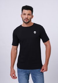 Black cotton t-shirt featuring short sleeves and a round neck, with a small white skull graphic on the left chest area.