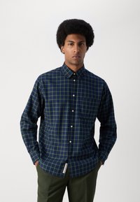 Karierte Button-Down-Bluse in Dunkelgrün und Marineblau, mit einer Brusttasche, abgerundetem Saum und kleinem Logotag am Saum. Aus Baumwolle.