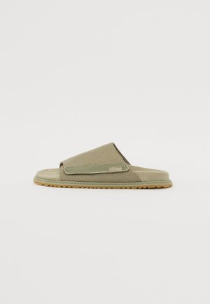 Sandale à glissière en tissu vert olive avec un design en bande croisée, semelle intérieure douce et semelle en caoutchouc. Présente une texture lisse et des accents minimalistes.