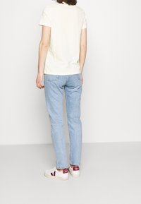 T-shirt jaune clair à manches courtes, associé à un jean bleu clair et des baskets blanches avec des accents rouges sur le talon.