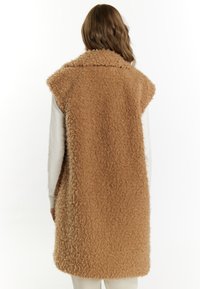 Nepbont vest in een warme beige kleur, met een hoge kraag, mouwloos ontwerp en een textuur met een onregelmatige afwerking.