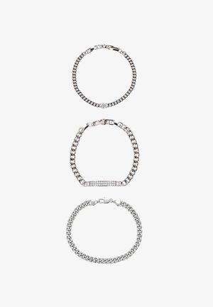 Tre braccialetti a catena d'argento: il superiore ha una chiusura rotonda con un cristallo, il centrale una barra rettangolare con strass, il inferiore è in stile classico a maglie.
