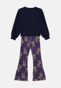Haut à manches longues bleu marine avec des manches bouffantes, associé à un pantalon violet évasé avec un imprimé animal audacieux en orange et noir.
