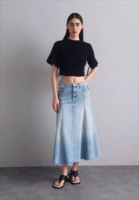 Maglione nero corto, maxi gonna in denim azzurro chiaro con orlo sfilacciato e sandali neri con una larga fascia. Design semplice e vestibilità comoda.
