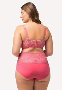 Růžový prádlo set obsahující krajkový bralet s nastavitelnými ramínky a odpovídajícími kalhotkami s vysokým pasem, ukazující květinový krajkový vzor.